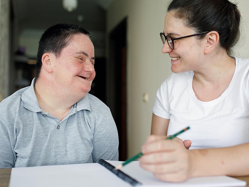 A young woman works with a young man on a work assessment. The woman is writing notes in a workbook. ©istockphoto.com