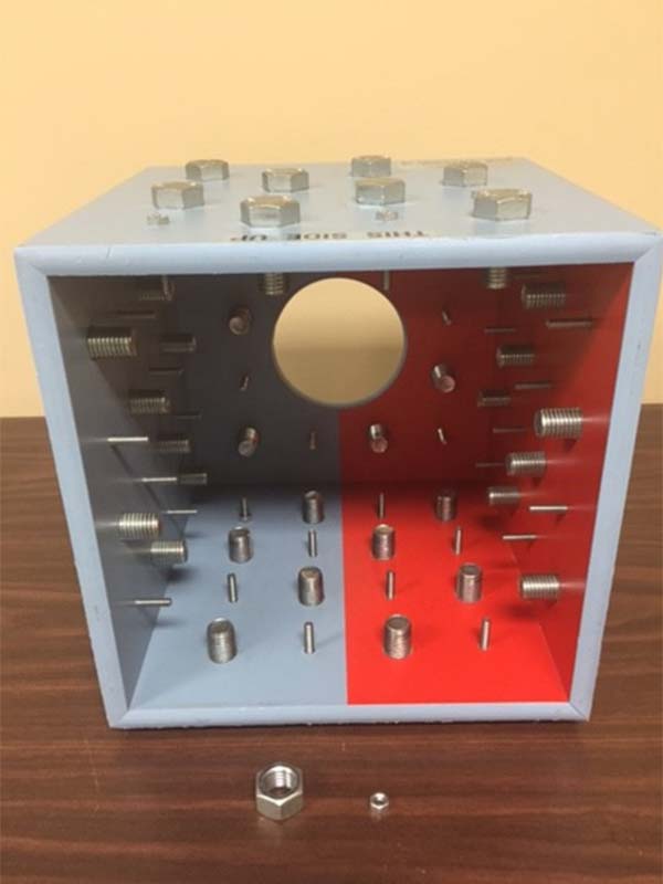 Tool used in the vocational assessment program to determine an individuals' upper extremity range of motion. Tool is a grey/red painted cube with a large number of bolts inserted through the bottom and side surfaces.